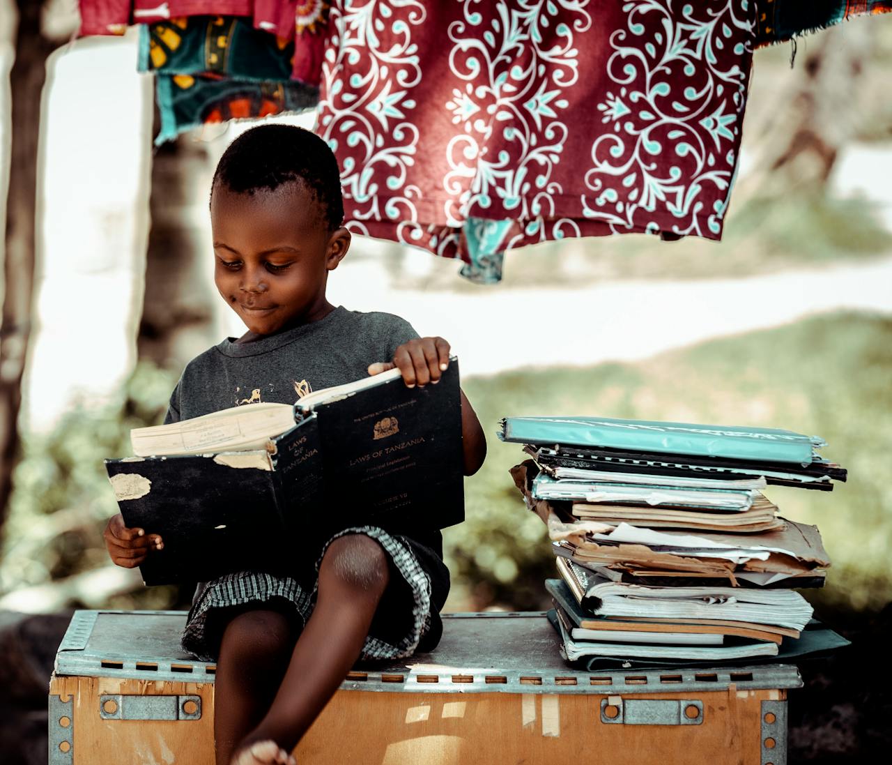 A young boy enjoys reading outdoors amidst a backdrop of colorful fabric in Tanzania.