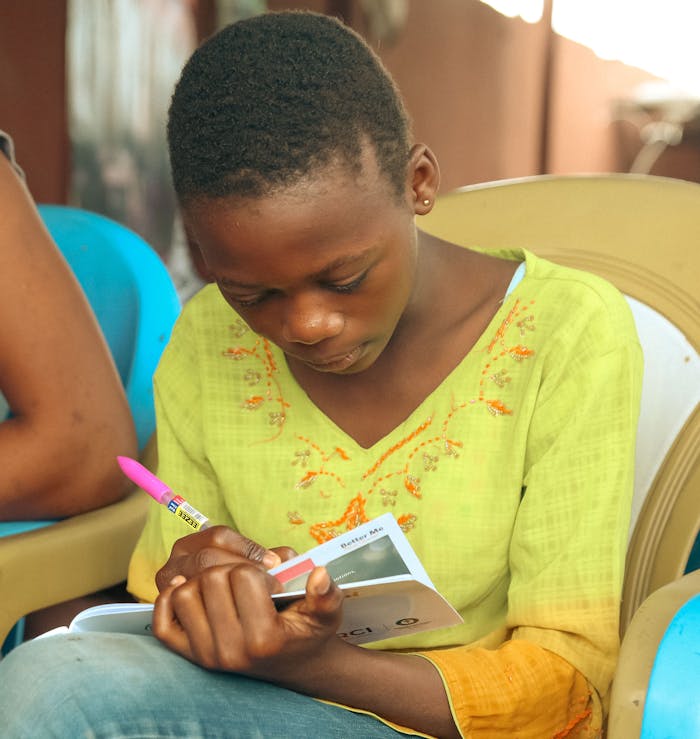 A young girl concentrates as she writes in her notebook while seated indoors.
