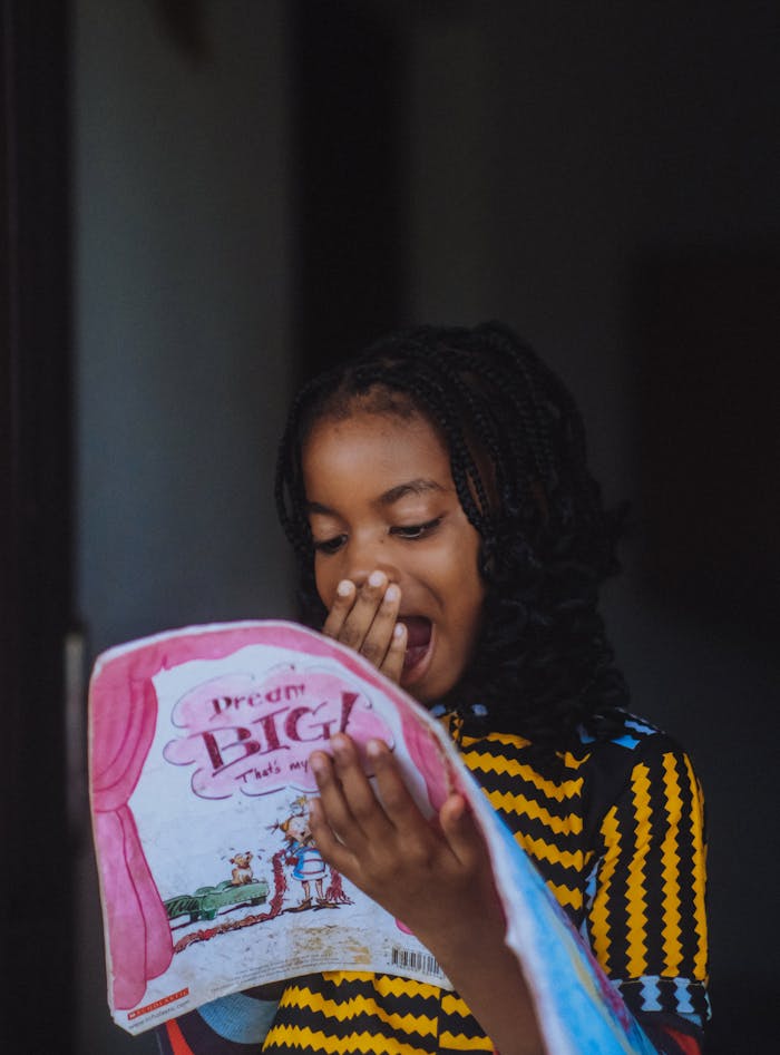A young girl reads a book with excitement, indoors, promoting education.