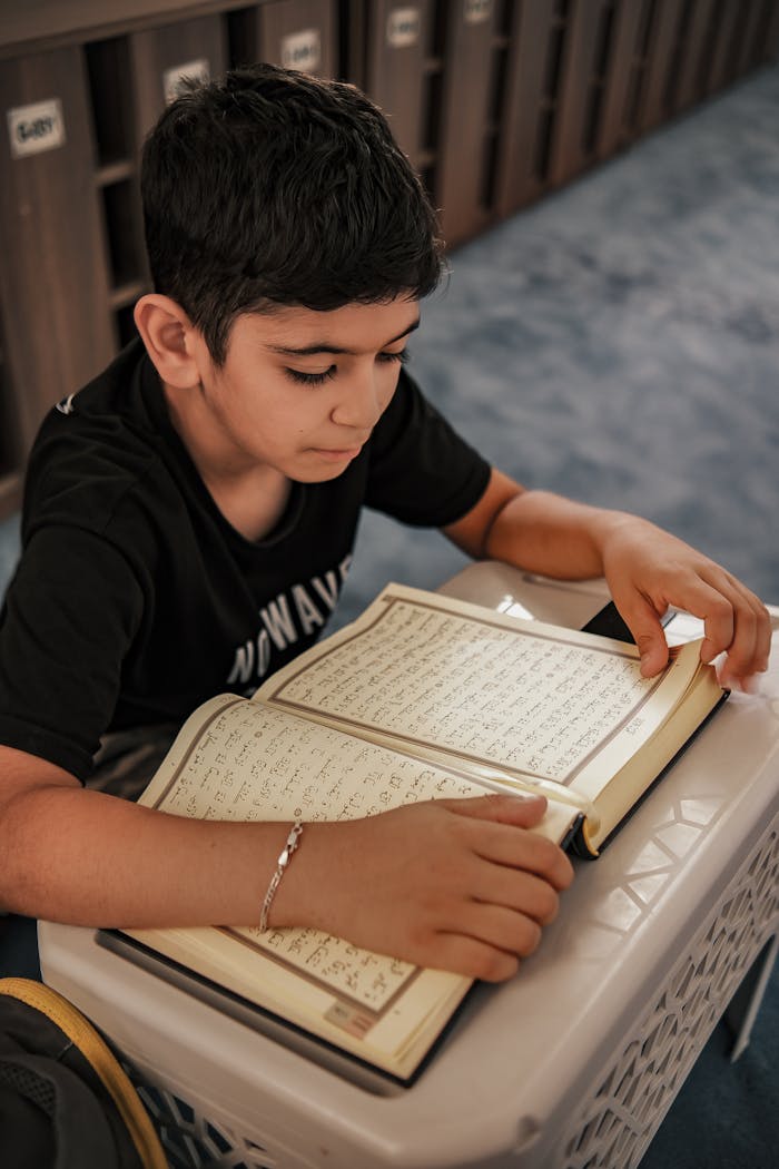 A young boy intently reading an open book indoors, focused and engaged.